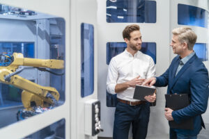 Two businessmen talking at robot in a modern factory